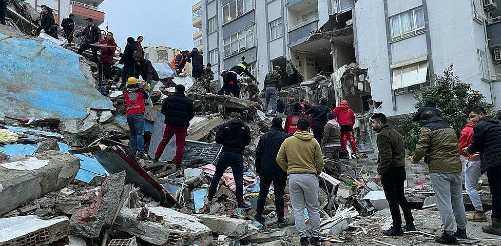 Betroffene des Erdbebens in der Türkei und in Syrien stehen vor den Trümmern eines eingestürzten Gebäudes