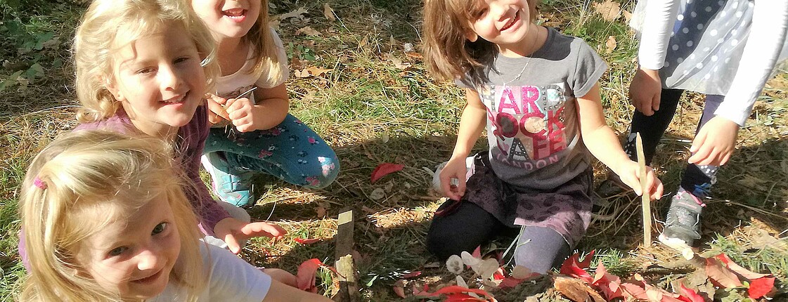 Kinder aus dem Caritas Kindergarten Unterfrauenhaid sitzen im Garten mit Blättern und Erde.