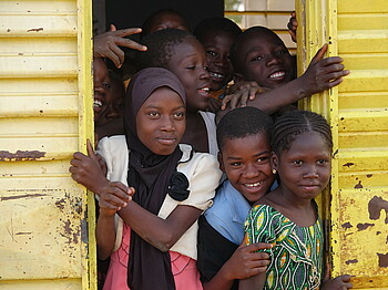 Ein Mädchen mit Kopftuch schaut mit einer Reihe anderer Kinder aus einem gelben Wagon.