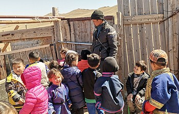 Eine Gruppe von Kindern vor einem Zaun, ein Erwachsener steht dabei