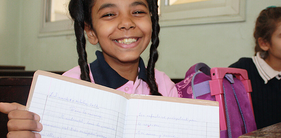 Ein ägyptisches Schulmädchen zeigt lachend ihr Schulheft.