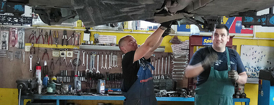 Das Bild zeigt zwei Männer, die an einem Auto arbeiten