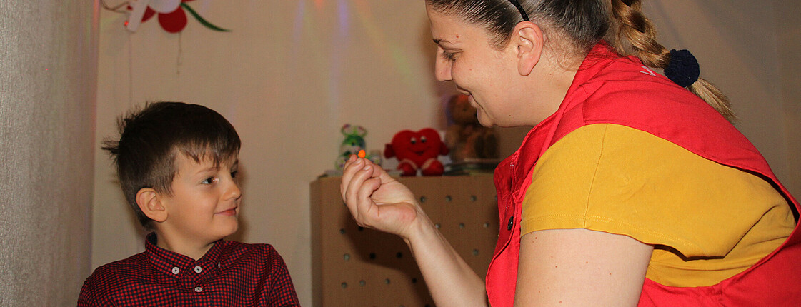 Eine Mitarbeiterin des Frühförderungszentrums in Kosovo bringt einem Jungen mit kleinen Steinen etwas bei.