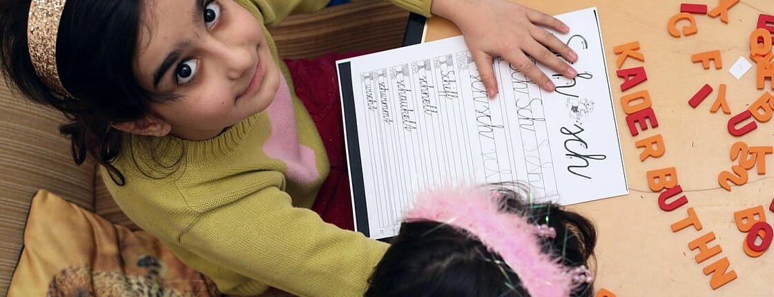 Ein Mädchen lernt mit Buchstaben und blickt zur Kamera hinauf.