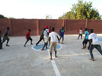 Viele Kinder beim Fußball spielen auf einem Fußballfeld aus Beton.