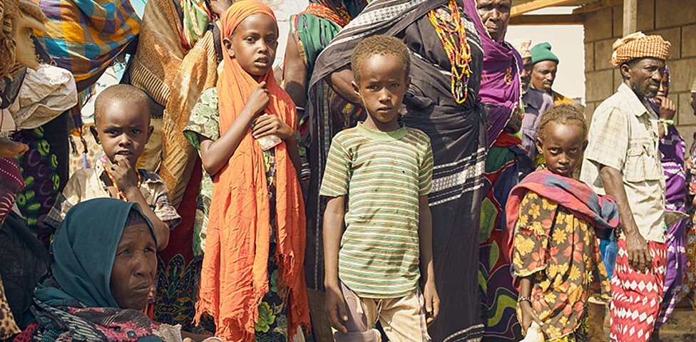 Eine Gruppe afrikanischer Kinder und Erwachsener warten auf die Verteilung von Lebenmitteln.