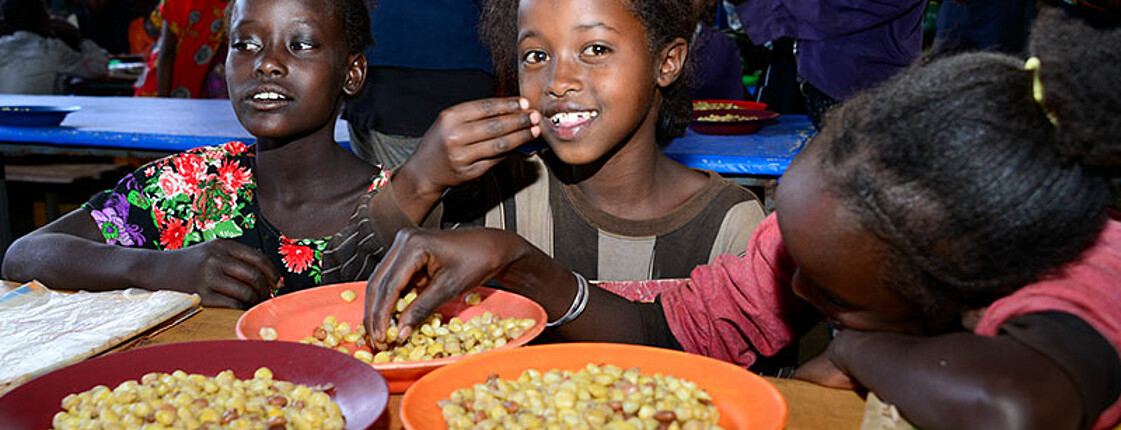Drei afrikanische Mädchen essen Bohnen.