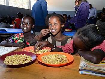 Drei afrikanische Mädchen essen Bohnen.