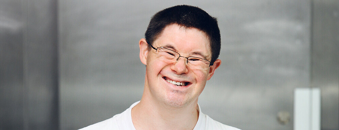 Mensch mit Behinderung lächelt und hält Teller in der Hand