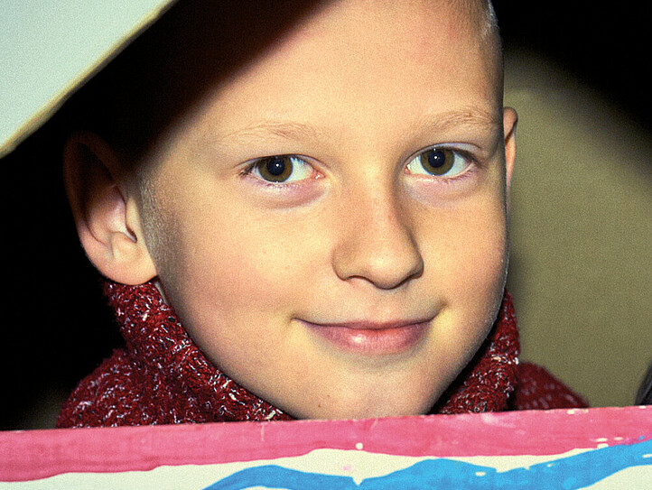 Das Bild zeigt ein Kind, das aus einem Pappkarton-Haus schaut