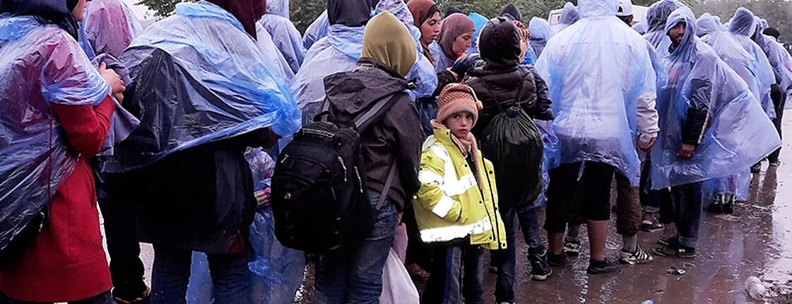 Flüchtlinge in Regenmänteln an der Grenze