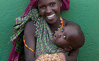 Frau mit Baby im Tragetuch und Getreide in der Hand