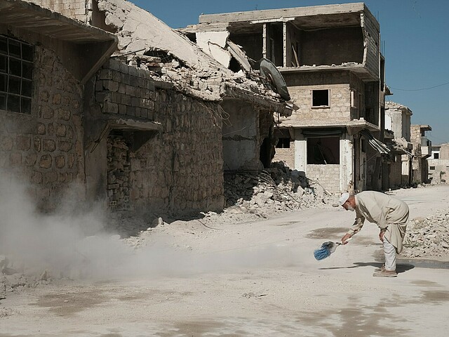 Es sind Ruinen von Häusern zu sehen, zerstört von den Erdbeben. Ein Mann steht gebückt auf der Straße und kehrt. 