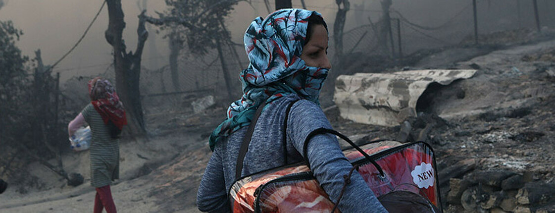 Frau geht schwer bepackt durch zerrüttete Straße
