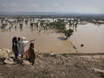 A person points towards their flooded home from a hilltop overlooking Nowshera