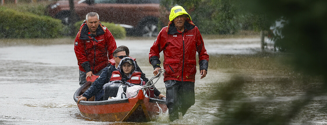 Menschen sitzen in einem Boot, sie werden bei Hochwasser evakuiert, es regenet.