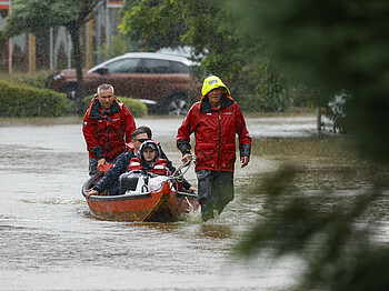 Menschen sitzen in einem Boot, sie werden bei Hochwasser evakuiert, es regenet.