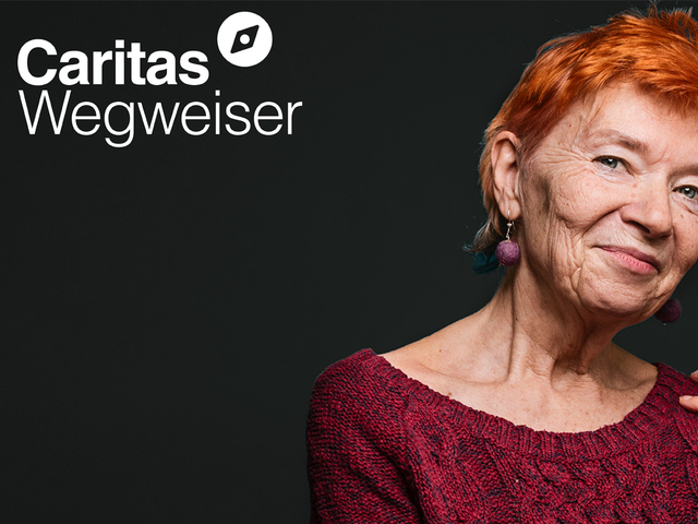 Das Porträt einer Frau ist zu sehen auf schwarzem Hintergrund. Es ist eine ältere Dame die lächelt, sie hat einen rothaarigen Kurzhaarschnitt. Links oben das Logo vom Caritas Wegweiser.