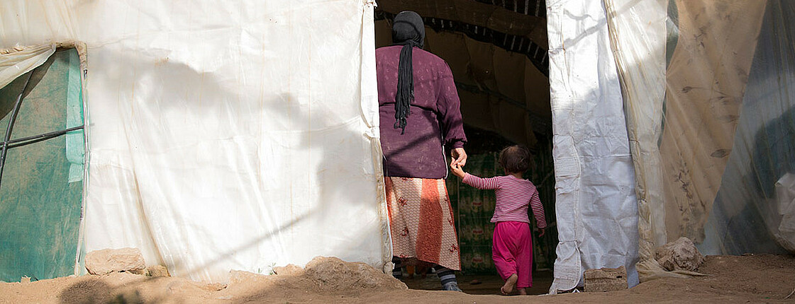 Frau und Kind halten sich an der Hand und gehen in ein Zelt