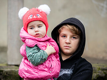 Junge mit Kapuze hält ein Kleinkind am Arm